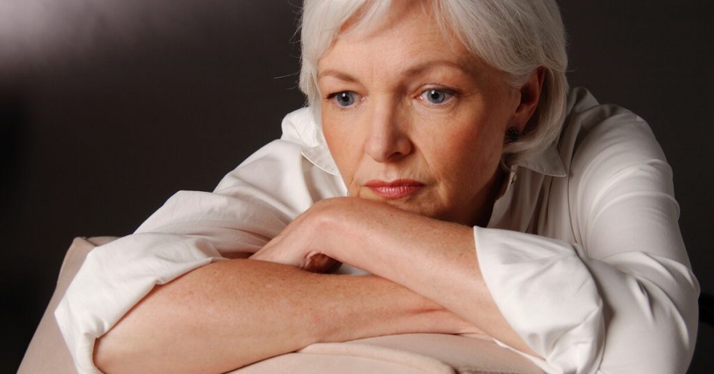 elderly woman resting her chin on her arms looking sad or in deep thought