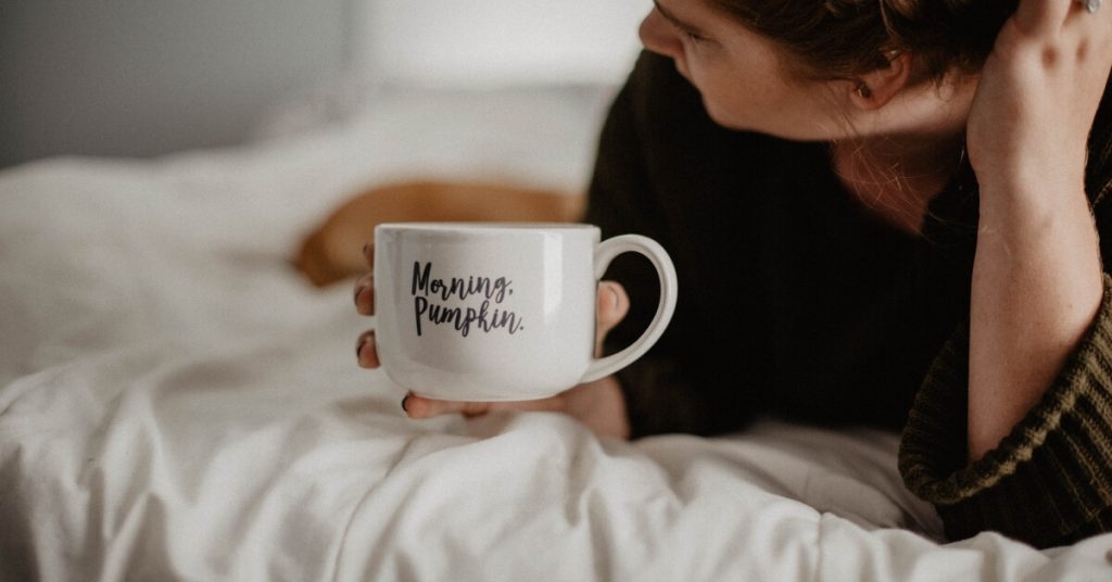 woman lying on bed with mug that has "morning pumpkin" on it 