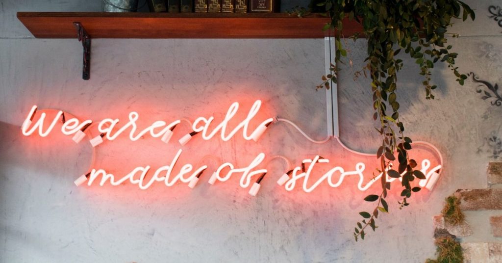 a neon sign on a wall which says we're all made of stories